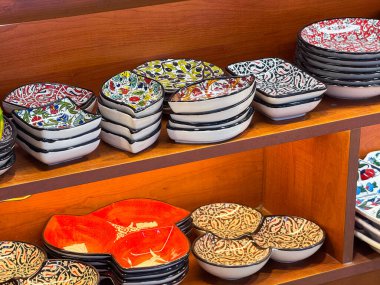 Ahşap raflarda seramik tabaklar ve çiçek desenleri var. Kültürel işçilik, dekoratif hizmetler ve günlük yaşamın zanaatkar mirası.