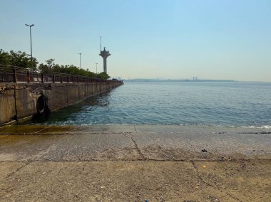 Arka planda uzun bir kule olan beton iskele denize doğru uzanıyor. Bakış açısına göre mimari, altyapı ve kentsel kıyı şeridi ortamı
