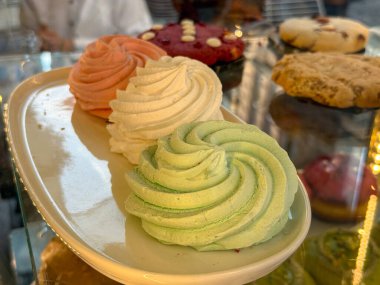 Fırın vitrininde beyaz bir tabağa dizilmiş renkli marşmelov girdapları. Tatlı şekerlemeler, zanaatkar tatlılar ve hoşgörüyü sembolize eden el yapımı kabarık tatlılar.