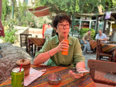 Kafe masasında oturan kadın samanla soda içiyor. Yaşam tarzı, boş zaman ve konukseverlik sosyal etkileşimi, kültürel atmosferi ve açık hava rahatlığını yansıtıyor.