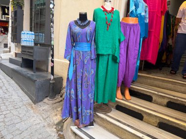 Bir dükkanın önünde renkli kıyafetler giymiş bir grup manken sergileniyor. Moda, kültür ve sokak perakende atmosferi