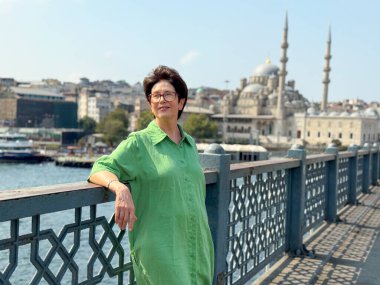 Yeşil elbiseli kadın Galata Köprüsü 'nden Boğaz' a bakıyor. Deniz kenarında tefekkür, seyahat ve şehir hayatı.