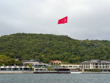 Liman manzaralı tepede büyük bir Türk bayrağı. İstanbul kentsel ve doğal ortamında sembolizm, vatanseverlik, kimlik ve ulusal gurur
