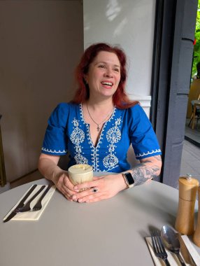 Kahve masasında kahve içen mavi işlemeli bir elbise giyen bir kadın. Yaşam tarzı, zarafet, rahatlık ve kentsel anlar