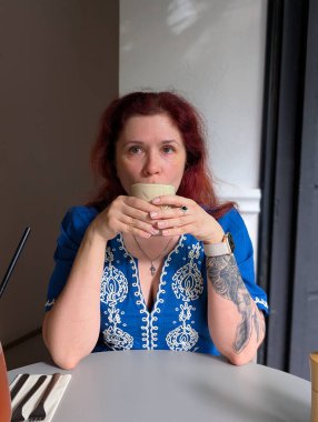 Kahve masasında kahve içen mavi işlemeli bir elbise giyen bir kadın. Yaşam tarzı, zarafet, rahatlık ve kentsel anlar