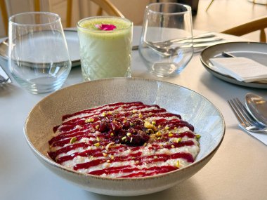 Masada bir kase kremalı puding, ahududu sosu ve ezilmiş şam fıstığı var. Tatlı, tatlı yemek ve modern yemek konseptinde yaratıcılık.