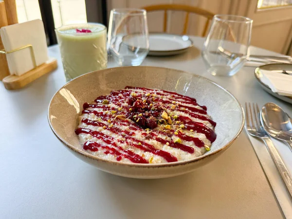 Masada bir kase kremalı puding, ahududu sosu ve ezilmiş şam fıstığı var. Tatlı, tatlı yemek ve modern yemek konseptinde yaratıcılık.