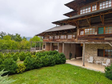 Bahçesinde çalılar olan ahşap bir kır evi. Geleneksel Sırp mimarisi, yeşillik ve kırsal atmosferi