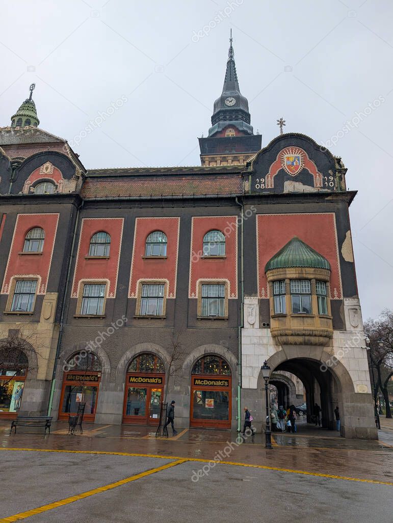 Main facade of Subotica City Hall with tower and public passage in Serbia. Urban culture, commercial presence and historic architecture blending heritage with modern retail environment
