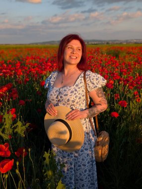 Bir kadın altın gün batımında haşhaş tarlasında hasır şapka tutarken gülümsüyor. Yaşam tarzı portre, duygusal cazibe ve doğa ile insan arasındaki uyumun güzelliği.