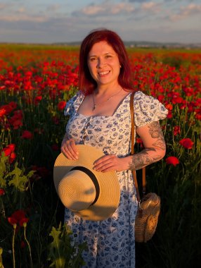 Bir kadın altın gün batımında haşhaş tarlasında hasır şapka tutarken gülümsüyor. Yaşam tarzı portre, duygusal cazibe ve doğa ile insan arasındaki uyumun güzelliği.