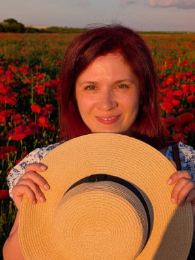 Bir kadın, haşhaş tarlasında dikilirken hasır şapkanın arkasına saklandı. Yaşam tarzı portresi, duygusal neşe ve bireysellik doğada ve kırsal alanda ifade edilir.