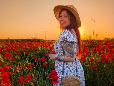 Neşeli bir kadın gün batımında gelincik tarlasında yürürken güler. Kırsal yaz manzaralı duygusal yaşam tarzı, güzellik ve bireysellik.