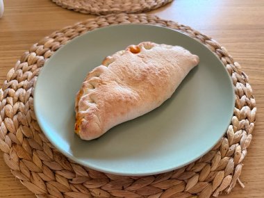 Altın kabuklu seramik tabağa yerleştirilmiş fırında calzone. Mutfak geleneği, Akdeniz mutfağı ve ev yapımı yemek ve kültürel gastronomi ile günlük yaşam tarzı