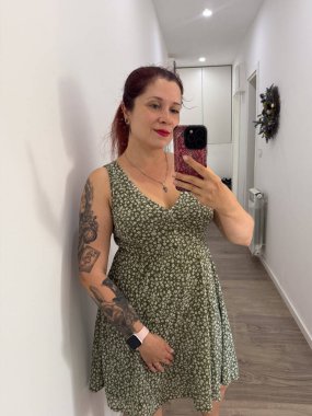 Dövmeli, yeşil çiçekli elbisesiyle selfie çeken bir kadın. Kişisel tarz, yaşam tarzı, moda ve kendini ifade etme güzellik, kimlik ve görünüş