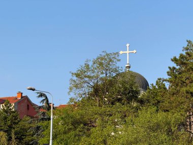 Mavi gökyüzüne karşı ağaçların üzerinde metal haç olan kilise kubbesi. Dini sembol, kültürel miras ve ruhaniyet, inanç ve kutsal simge içeren toplum kimliği.