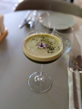 Kafe masasında garnitürle servis edilen yeşil bir kokteyl. Mutfak sanatı, yaşam tarzı tazeleme ve modern yemek ortamında miksoloji kültürü.