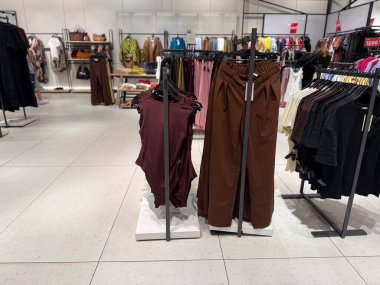 Pantolon ve üstler diğer bölümlerle çevrili bir perakende mağazasında raflara dizilir. Moda ticareti, tüketici talebi, mevsimsel tarz ve modern alışveriş endüstrisinde tekstil ticareti