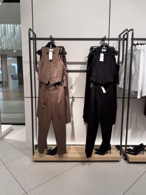 Tarafsız renklerde resmi pantolon ve yelekler bir perakende mağazasında askılarda sergilenir. Modern alışveriş kültüründe giysi ticareti, tüketici talebi, tekstil ticareti ve moda endüstrisi