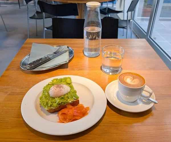 Bir kafede servis edilen bir tabakta haşlanmış yumurta ve somon balıklı avokado tostu. Sağlıklı kahvaltı, taze malzemeler ve gurme yemekleri.