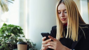Genç sarışın kız kafede masada bir akıllı telefon sittig ile çalışır