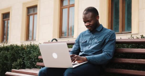 Afrikanisch-amerikanischer Geschäftsmann sitzt auf der Bank und arbeitet an seinem Laptop — Stockvideo