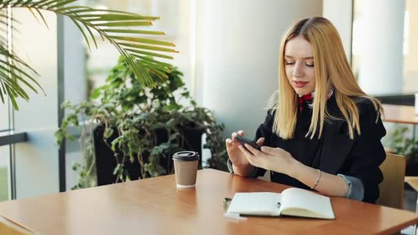 Young businsess woman types something in her smartphone sitting in cafe — Stock Video