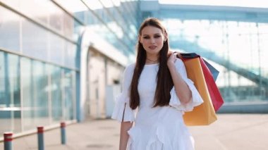 Beyaz elbiseli güzel moda model modern Cam bina önce alışveriş torbaları ile poz veriyor