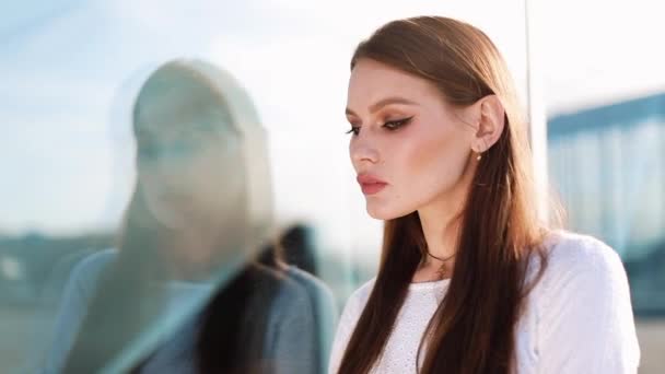 Young woman looks at her reflecion in the glass wall and then turns to the camera — Stock Video