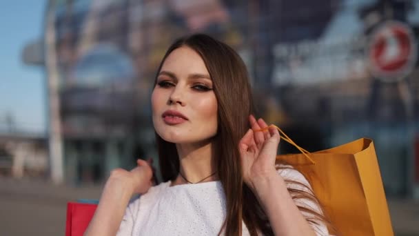 Krásná modelka v bílých šatech představuje s nákupní tašky před budovou moderního skla — Stock video