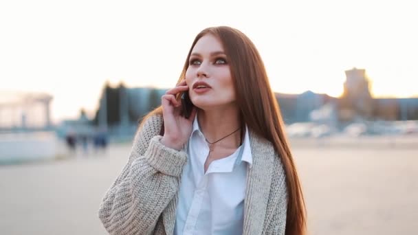 Ung kvinna med långt hår går längs gatan och pratar i telefon — Stockvideo