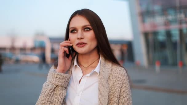 Ung kvinna med långt hår går längs gatan och pratar i telefon — Stockvideo