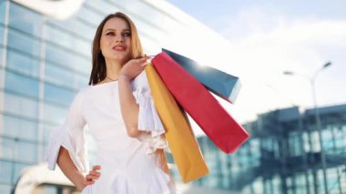 Beyaz elbiseli güzel moda model modern Cam bina önce alışveriş torbaları ile poz veriyor