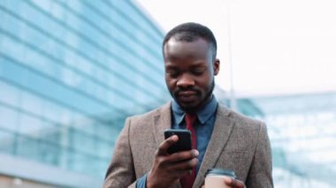 Afrika kökenli Amerikalı adam bir şey dışında yürüyüş onun smartphone içinde türleri. Businesman Havaalanı terminal, kullanır onun telefon, kahve içmek yürür, baskı mesaj, gülümsüyor. Neşeli ruh mutlu olmak,
