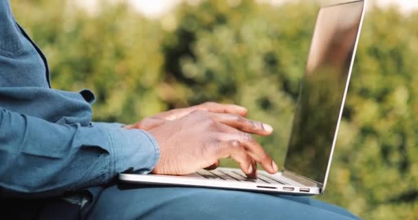 Primer plano de las manos de un joven negro. Él está usando una camisa y escribiendo en el teclado de su computadora portátil. Concepto de trabajo independiente. Bloqueado en tiempo real tiro de cerca — Vídeo de stock