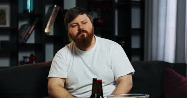 Sakallı şişman adam ayı içecekler ve Mısır ile masadan elinde uzaktan kumanda ile Tv izliyor