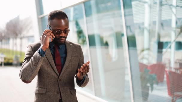 Africano americano homem chama alguém em seu smartphone de pé perto do centro de escritório — Vídeo de Stock