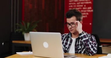 Ciddi genç iş adamı kendi dizüstü kullanarak modern ofiste çalışan bardaklarda portresi