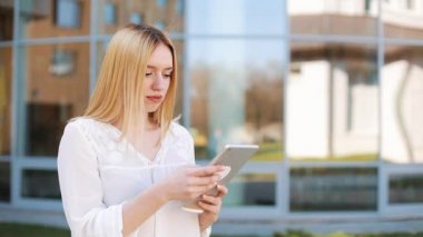 Tablet bilgisayar aygıtı dışında sokakta kullanan genç ve güzel sarışın kadın. Kadın gülümsüyor, dokunmatik ekran dokunarak, tarassut video, haber