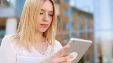 Tablet bilgisayar aygıtı dışında sokakta kullanan genç ve güzel sarışın kadın. Kadın gülümsüyor, dokunmatik ekran dokunarak, tarassut video, haber