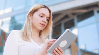 Tablet bilgisayar aygıtı dışında sokakta kullanan genç ve güzel sarışın kadın. Kadın gülümsüyor, dokunmatik ekran dokunarak, tarassut video, haber
