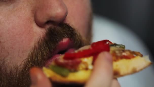 Gordo com barba come pizza sentada à mesa com cerveja e pipoca antes de um televisor — Vídeo de Stock