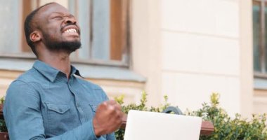 Dizüstü bilgisayarda çalışarak çekici Afrikalı-Amerikalı adam bankta oturur. Heyecanlı ve mutlu iyi haber aldı. Uzaktan serbest çalışıyorum. Başarı kavramı