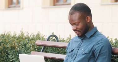 Dizüstü bilgisayarda çalışarak çekici Afrikalı-Amerikalı adam bankta oturur. Heyecanlı ve mutlu iyi haber aldı. Uzaktan serbest çalışıyorum. Başarı kavramı