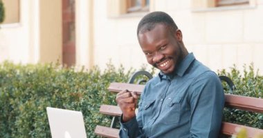 Dizüstü bilgisayarda çalışarak çekici Afrikalı-Amerikalı adam bankta oturur. Heyecanlı ve mutlu iyi haber aldı. Uzaktan serbest çalışıyorum. Başarı kavramı