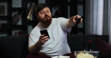 Şişman adam Tv ve türleri bir şey onun smartphone içinde izliyor. Eve yemek siparişleri. Yetersiz beslenme, gıda dağıtım, geri kalan kavramı