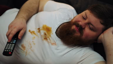 Oturma odasında onun kanepede televizyon izlerken kirli T-shirt gülüyor şişko adam