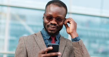 Çekici Afro-Amerikan Bussinessman office cente sokakta yakınındaki ayakta kulaklık müzik dinlemek. O şehirde ve ritmine dans smartphone kullanarak