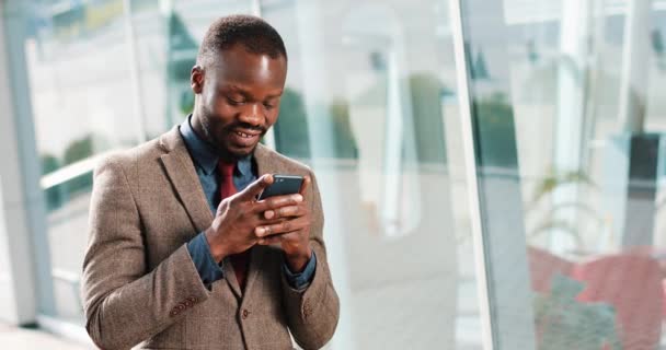 Ελκυστική αφρικανική αμερικανική άνθρωπος χρησιμοποιώντας smartphone στην πόλη. Όμορφος νεαρός επιχειρηματίας γραπτών μηνυμάτων sms χρησιμοποιώντας app χαμογελά ευτυχισμένη. Αυτός στέκεται κοντά στο Καϊμάκτσαλαν γραφείο στην οδό — Αρχείο Βίντεο