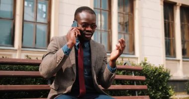 Bir bankta oturan genç Afrikalı-Amerikalı adam ve onun smartphone üzerinde görüşmeler. İş ortağı konuşuyor. İş ve yaşam tarzı kavramları.